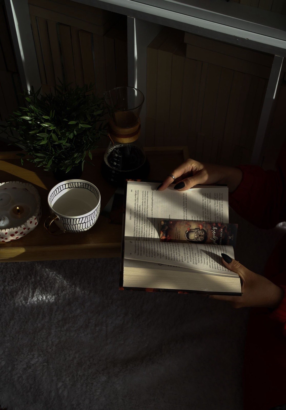 A cup of tea, a lit candle, and an open book resting on a sunlit windowsill nook.