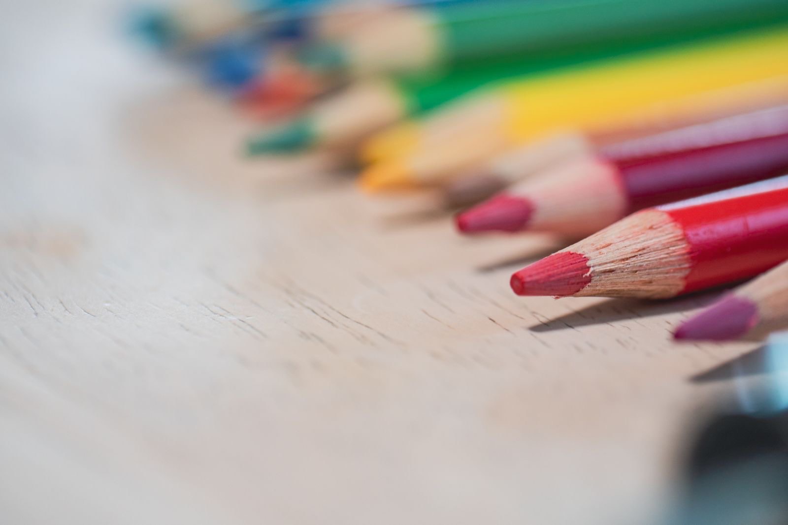 A row of colored pencils with sharpened tips lined up on a light wooden table.